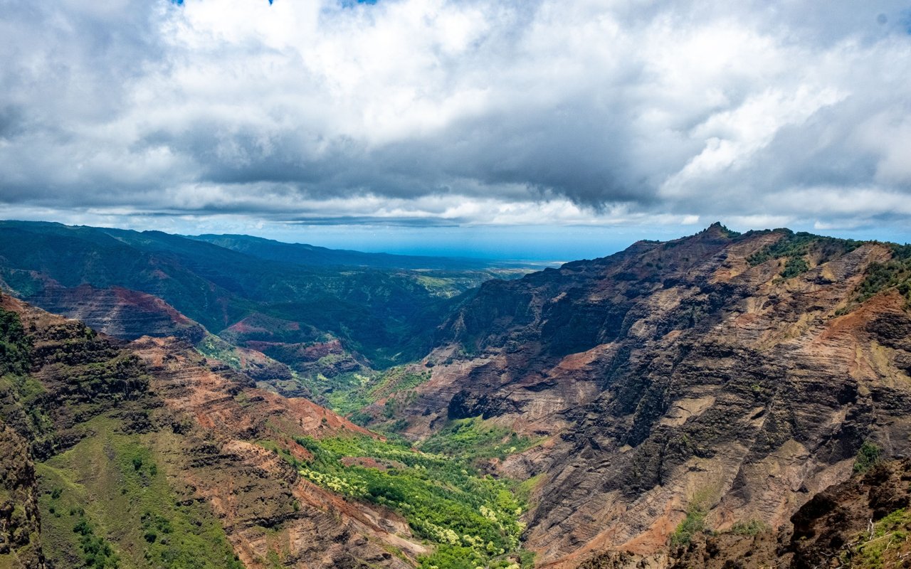 Rugged green valley between reddish-brown ridges beneath a broad, cloudy sky.