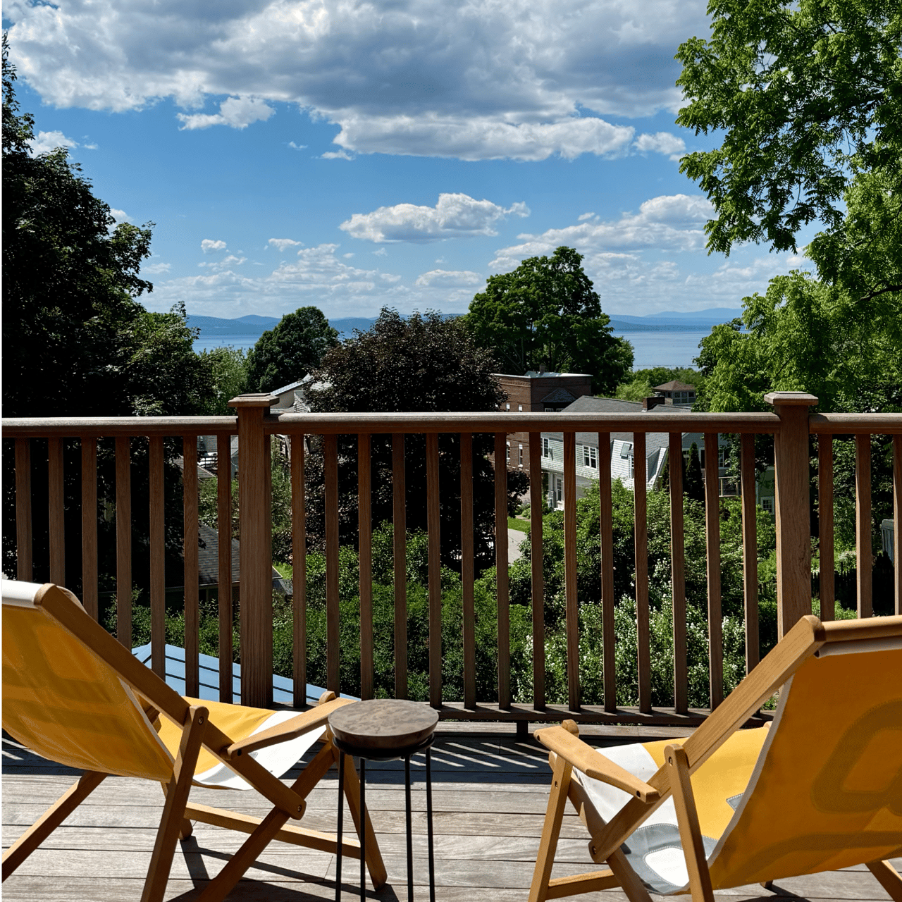 Wooden deck with yellow lounge chairs overlooking a lake and distant mountains.
