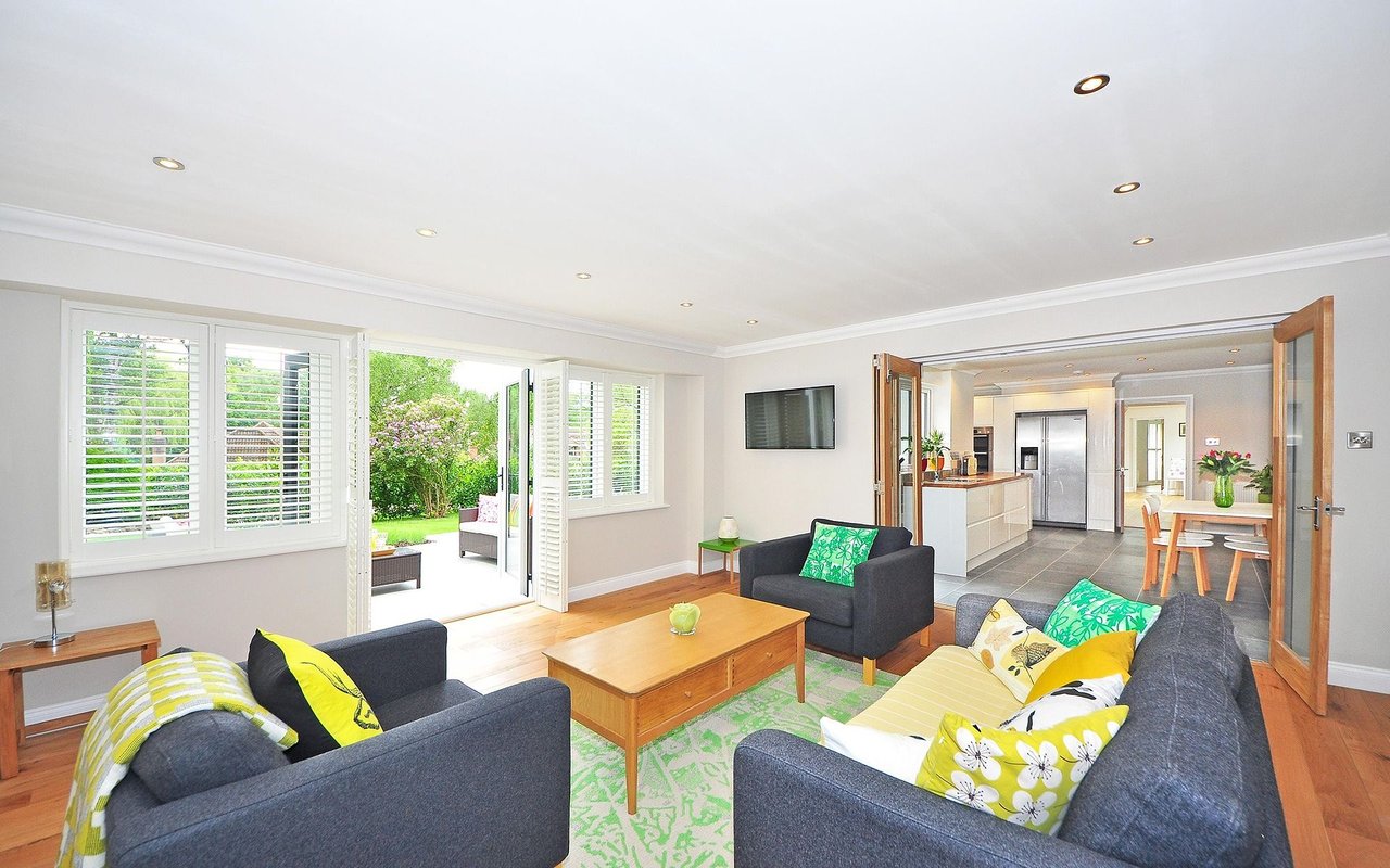 Furnished living room with gray sofas and open doors to a garden, connected to a modern kitchen and dining area.