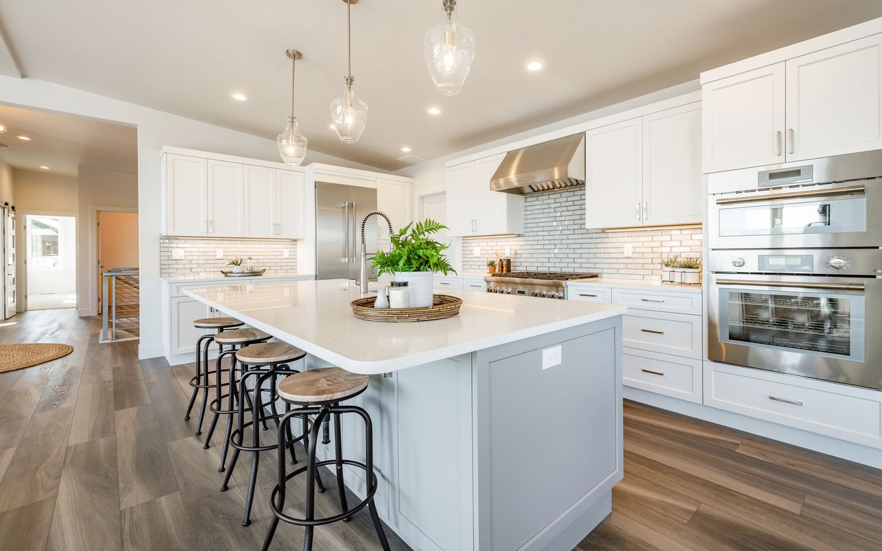 Modern white kitchen with a large island, bar stools, and stainless steel appliances.