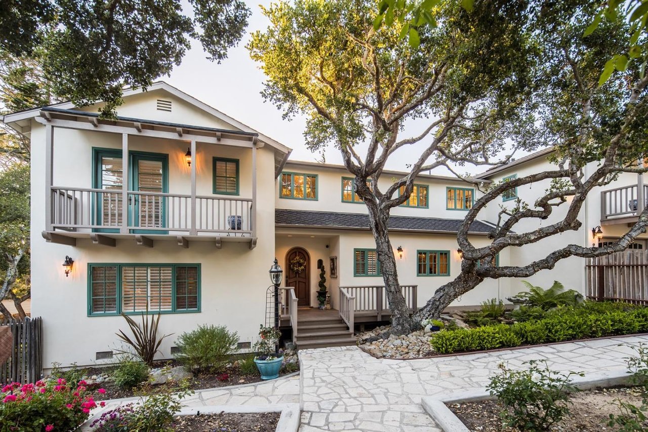 White two-story home with green-trimmed windows, balconies, and a large tree in front.