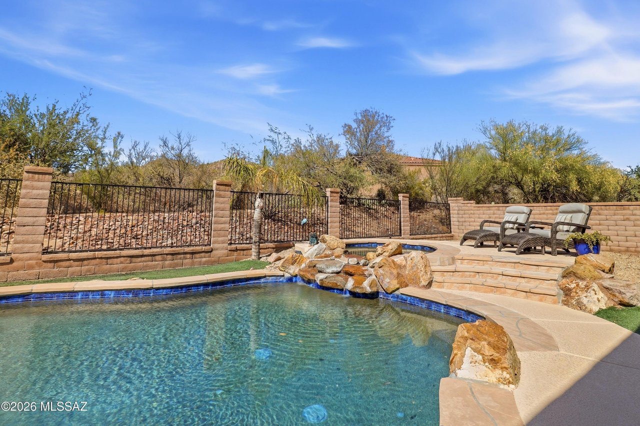 Desert backyard pool with a rock waterfall, curved blue-tile edge, and two lounge chairs.