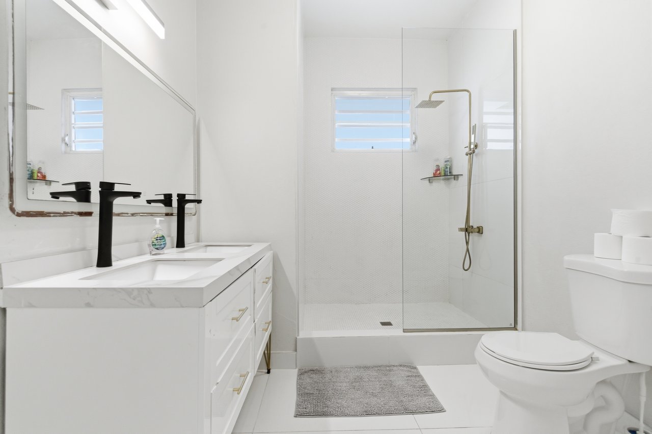 Bathroom with a double-sink vanity and glass walk-in shower with brass fixtures.