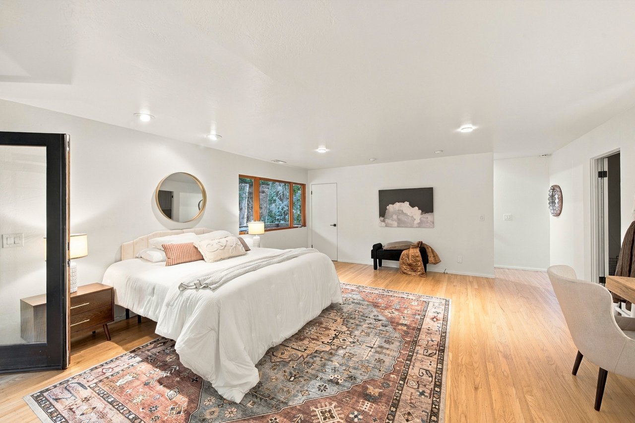 Bedroom with a white bed, patterned rug, hardwood floors, and large windows.