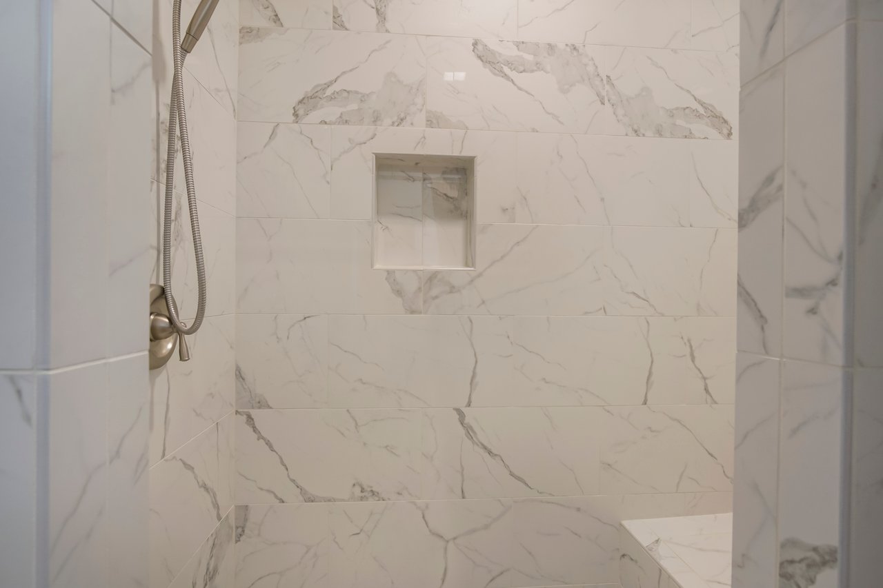 Marble-tiled shower with a built-in niche and a handheld showerhead. The clean, elegant design conveys a modern and serene bathroom atmosphere.