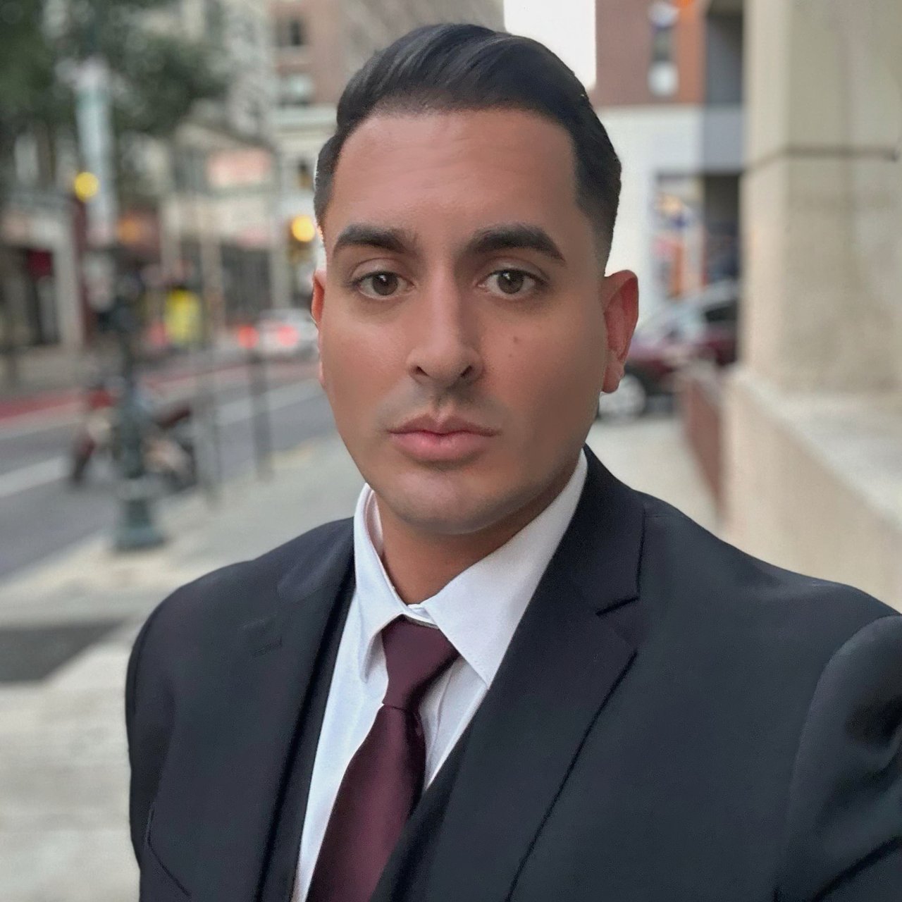 Salvatore Cognat in a dark suit and burgundy tie against a blurred city street.