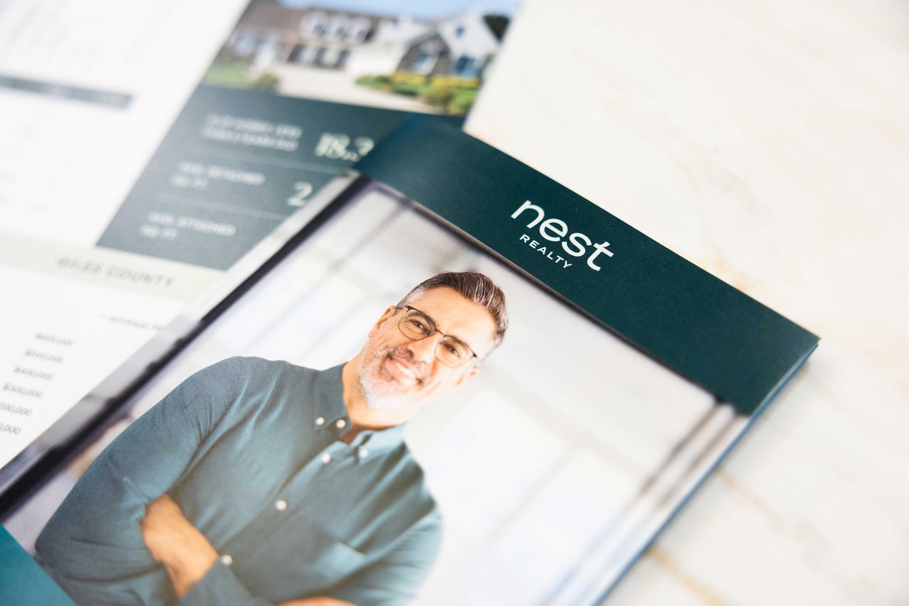 brochure on a table featuring photo of an agent and the Nest Realty logo