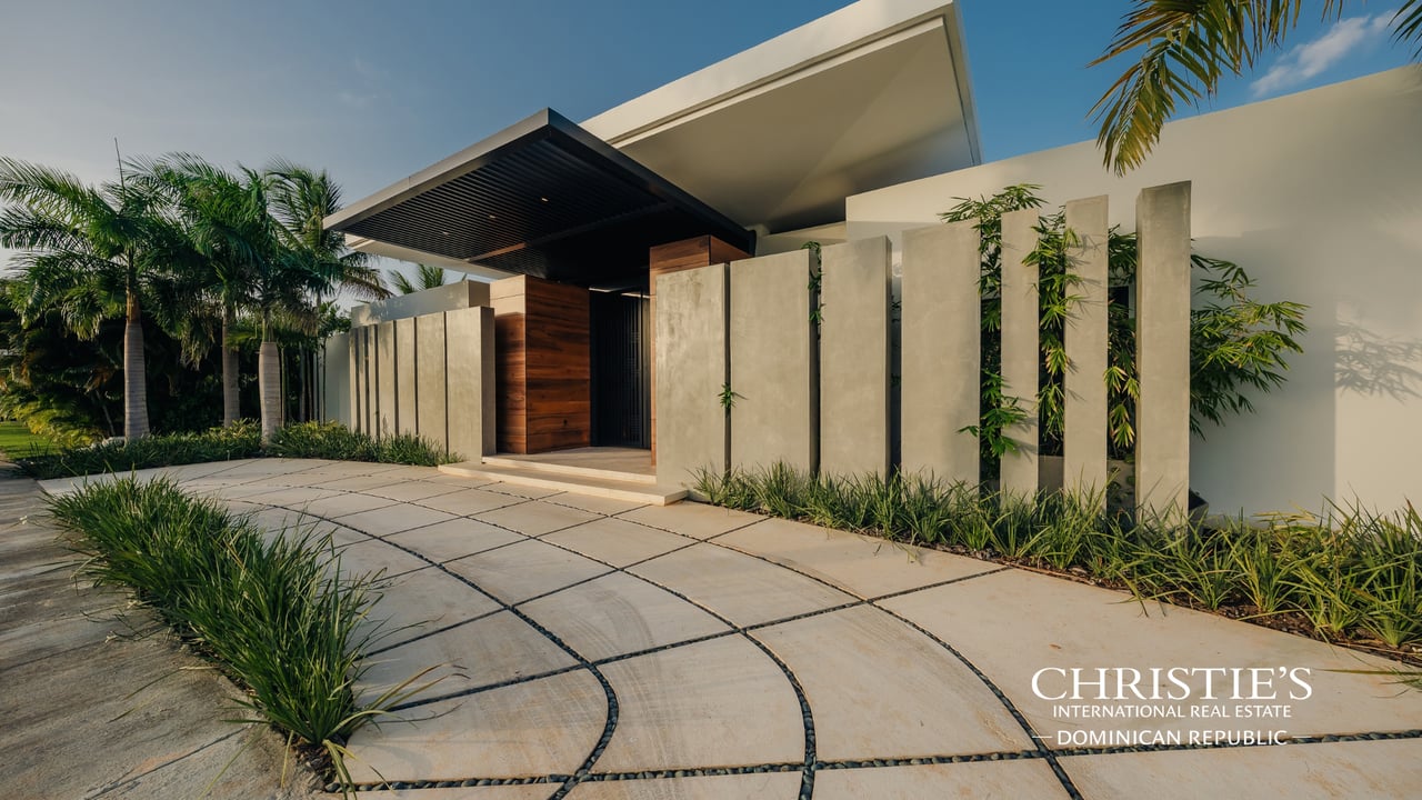 Modern villa entrance with concrete privacy fins, a dark canopy, and tropical landscaping.
