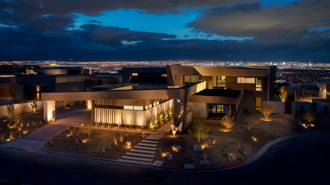 Modern luxury home at night overlooking the Las Vegas city lights, with illuminated landscaping.