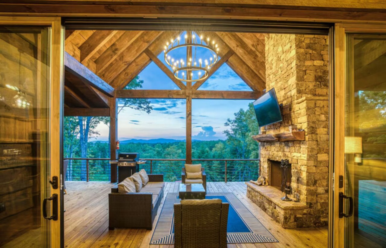 Covered timber deck with lounge seating, stone fireplace, and forested mountain views.