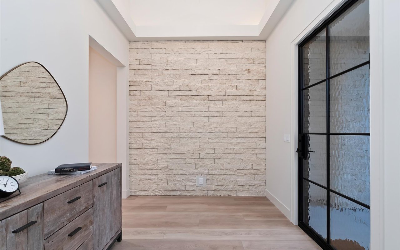 New construction modern prairie home. Foyer with black steel front door, stone accent wall, tray ceiling, and LVP flooring.