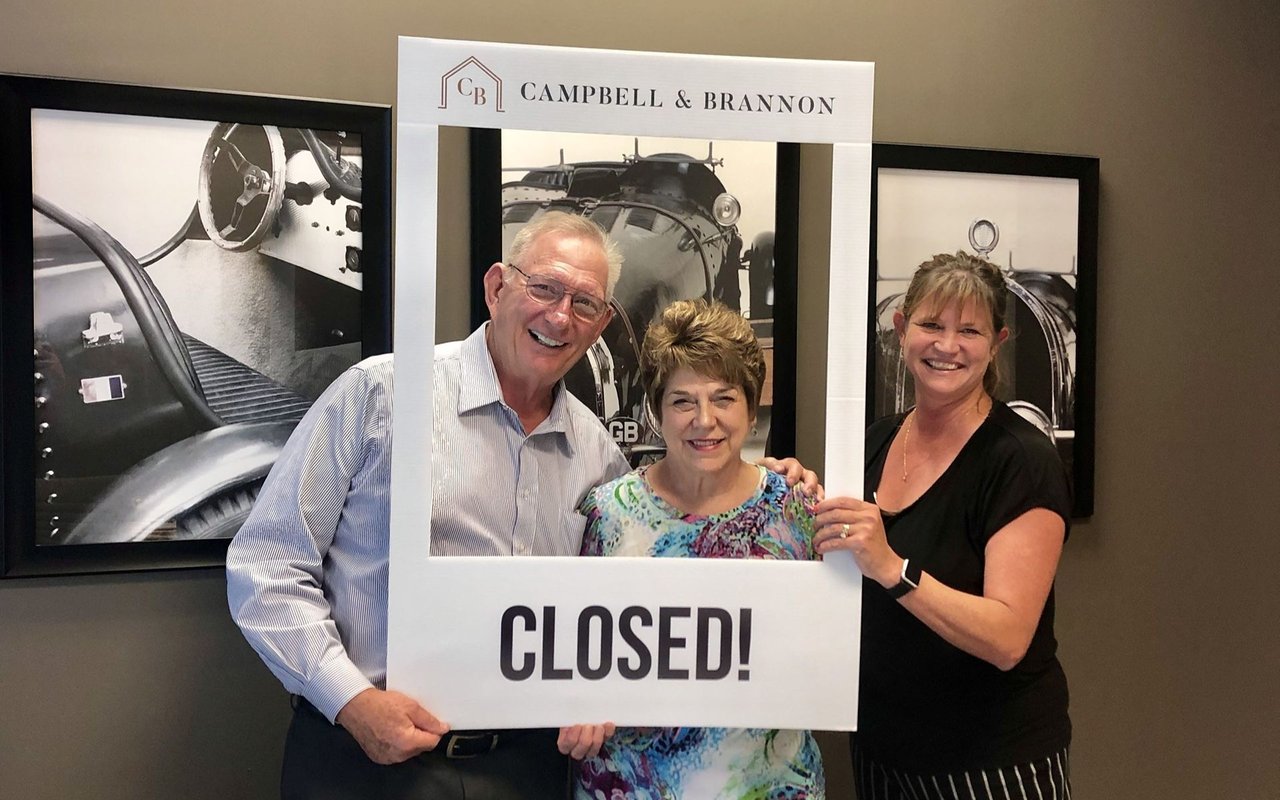 A couple and their agent pose with a large “CLOSED!” sign.