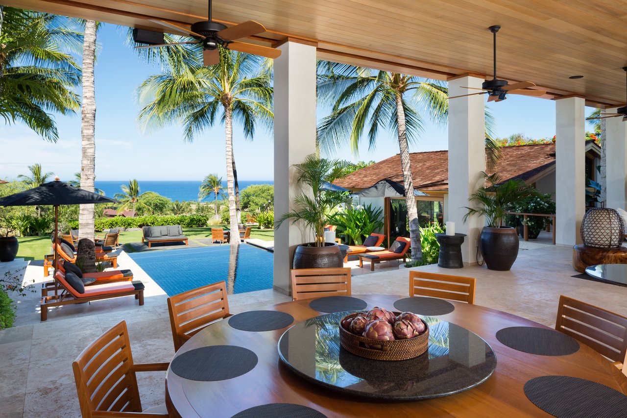 Covered patio dining area overlooking a pool, palm trees, and the ocean.