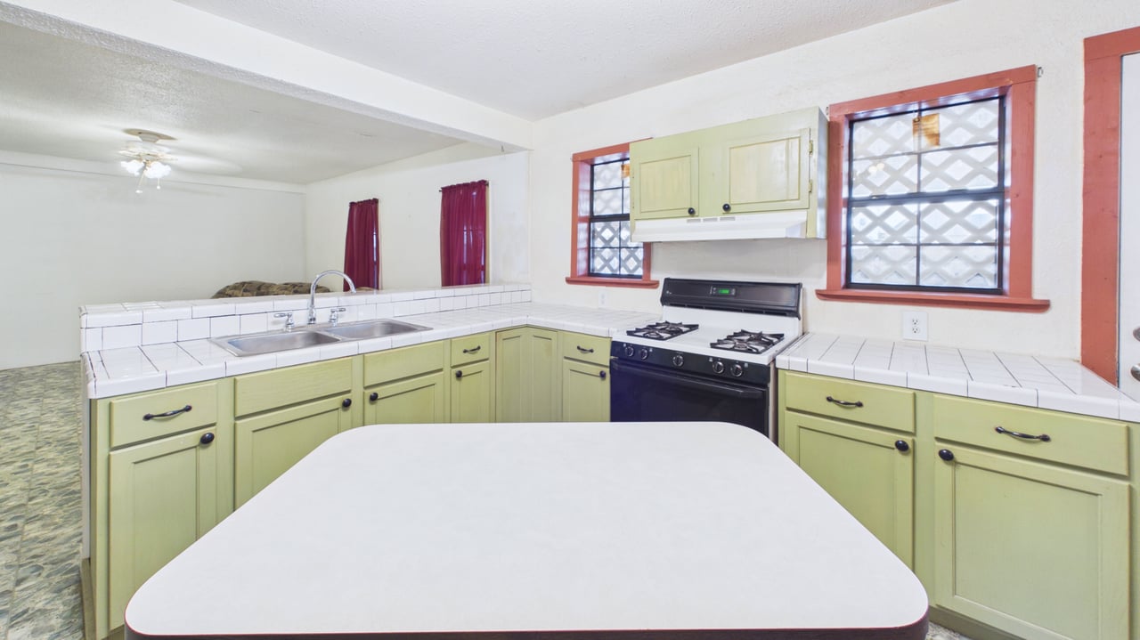 Kitchen with pale green cabinets, white tiled counters, a gas range, and red-trimmed windows.