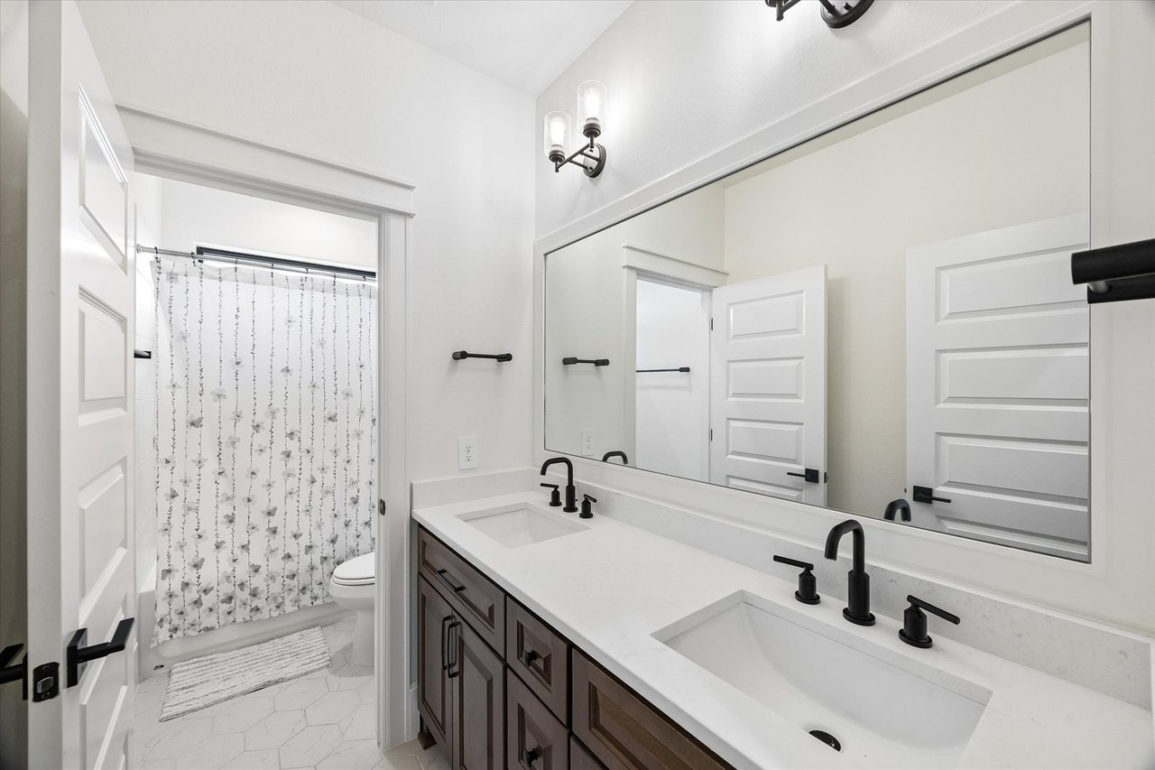 Bathroom with a double-sink vanity, dark cabinetry, large mirror, and patterned shower curtain.