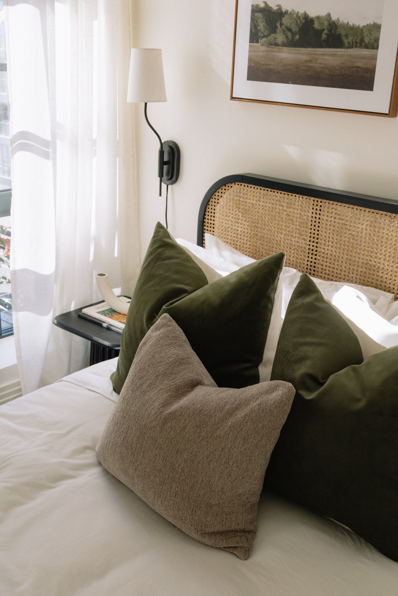 Bedroom with a cane headboard, olive green pillows, and sheer curtains.
