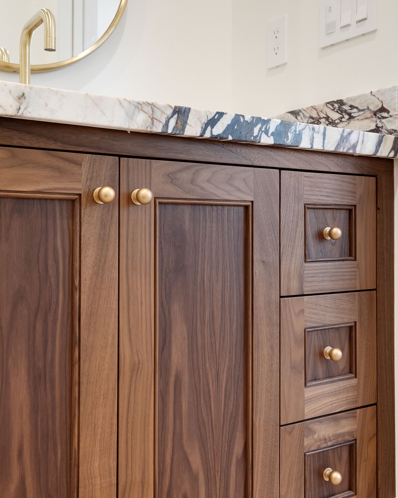 Bathroom vanity with walnut cabinets, brass knobs, and a blue-veined marble countertop.