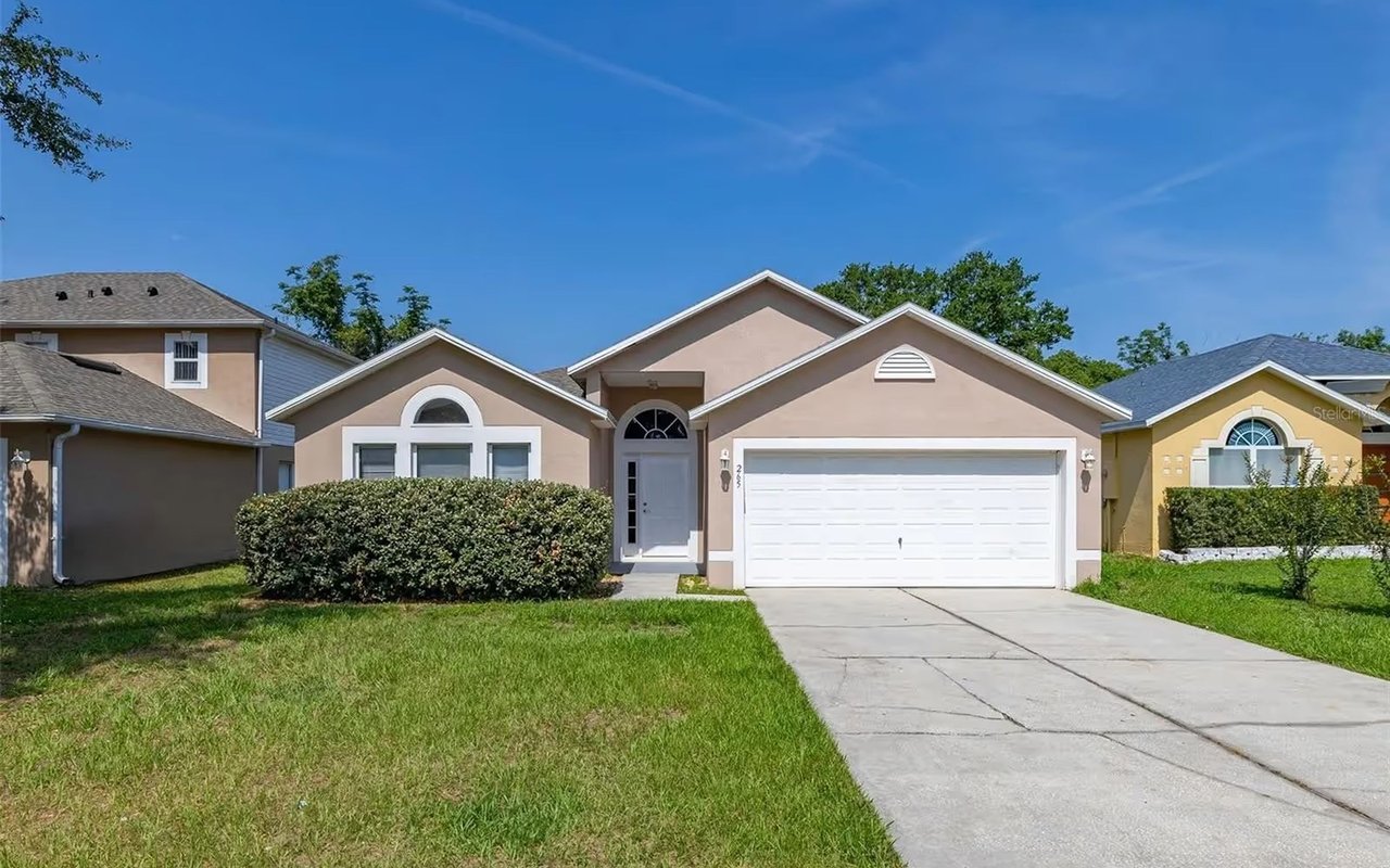 Peach single-story home with a white double garage, arched entry, front lawn, and driveway.