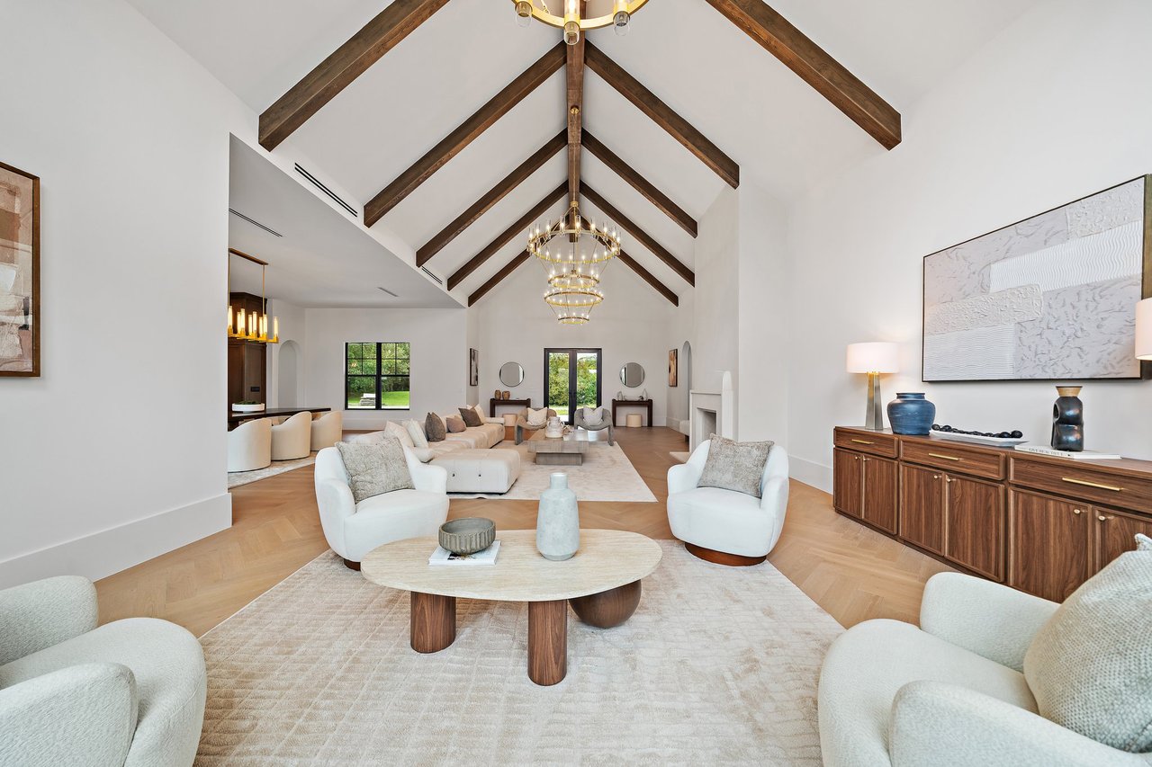 Vaulted living room with exposed wood beams, chandelier, white seating, and a fireplace.