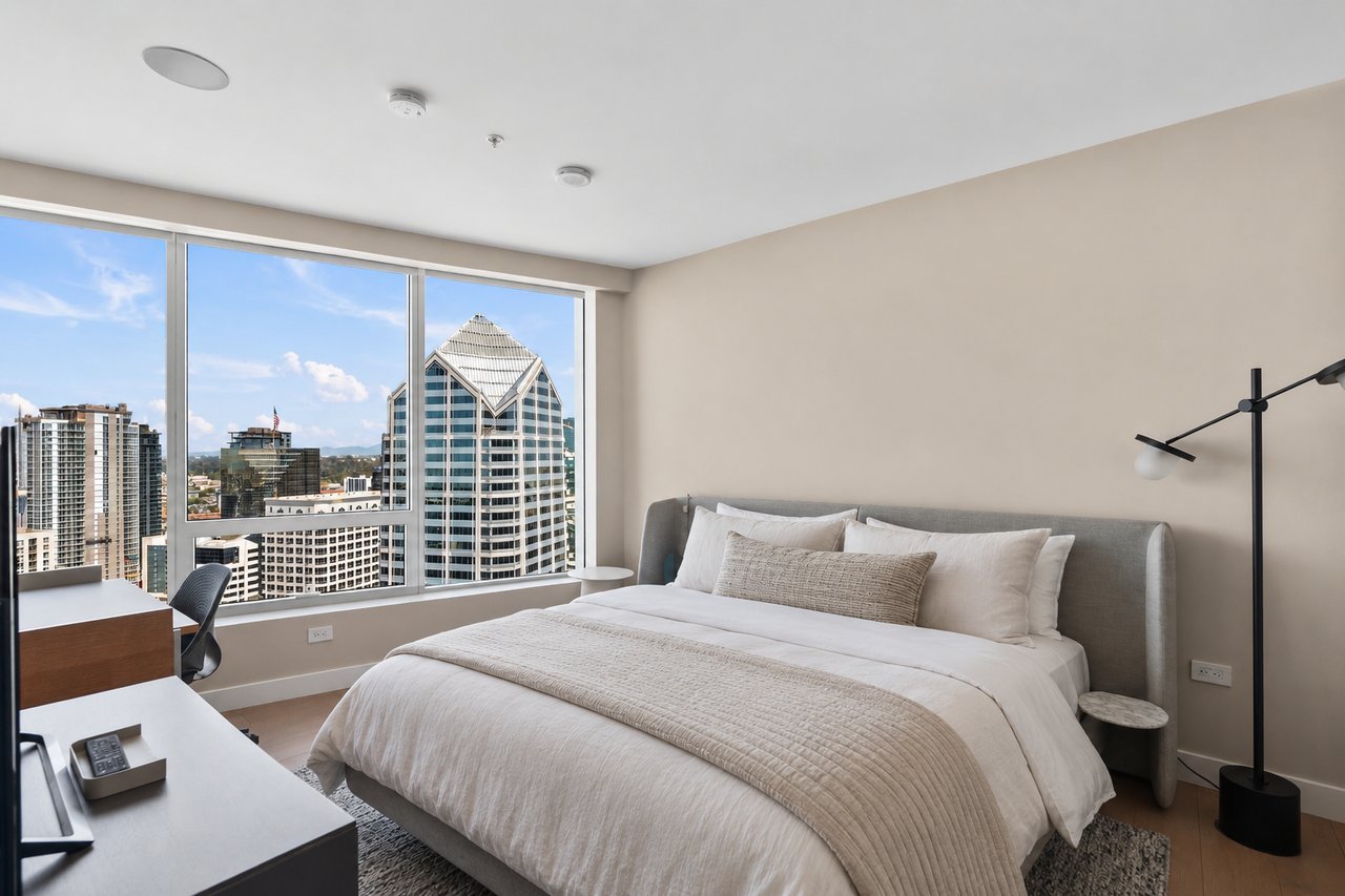 Furnished bedroom with a large bed and floor-to-ceiling windows overlooking the downtown skyline.