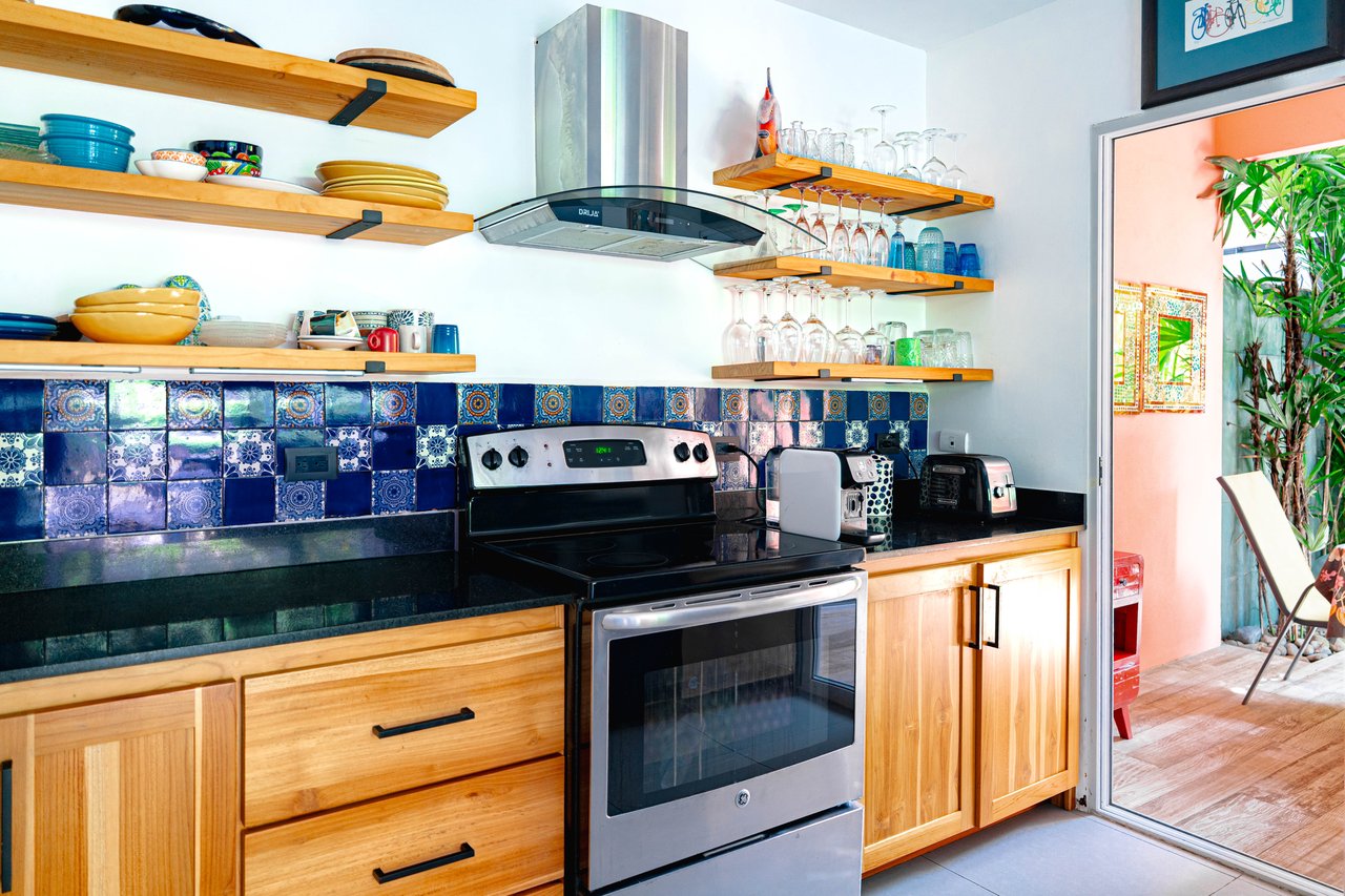 Kitchen with blue patterned tile backsplash, open wood shelves, and stainless steel range beside a patio door.