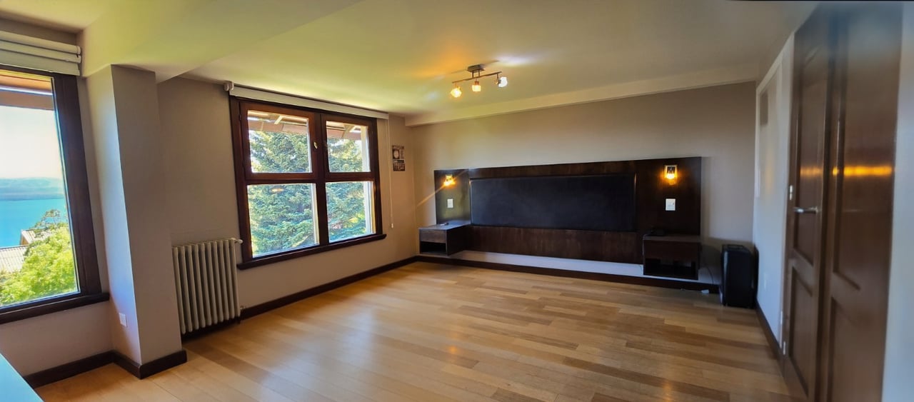 Empty bedroom with a built-in dark headboard and windows overlooking water and trees.