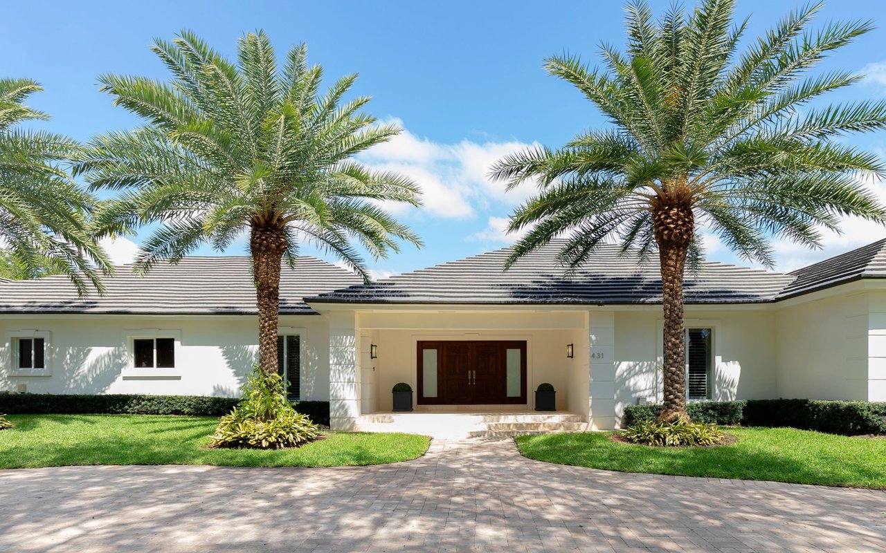 White single-story home framed by two tall palms, with a covered entry and paved driveway.