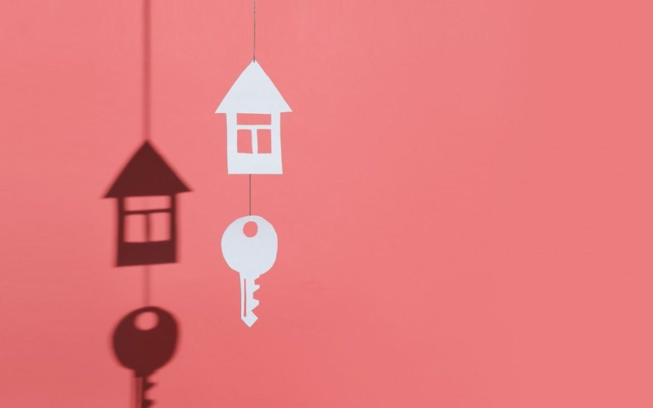 Paper house and key cutouts cast shadows on a coral-pink background.