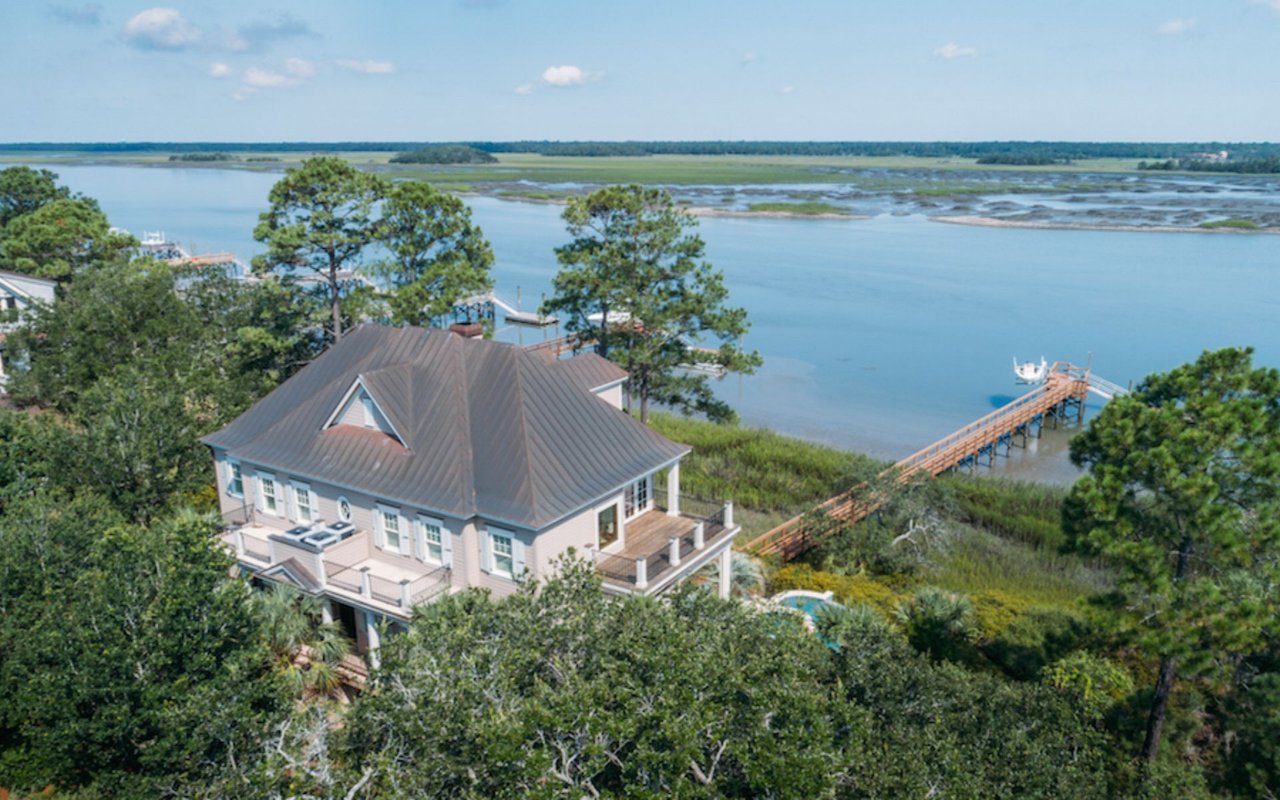Aerial view of a riverfront home with a long dock extending over marsh water.
