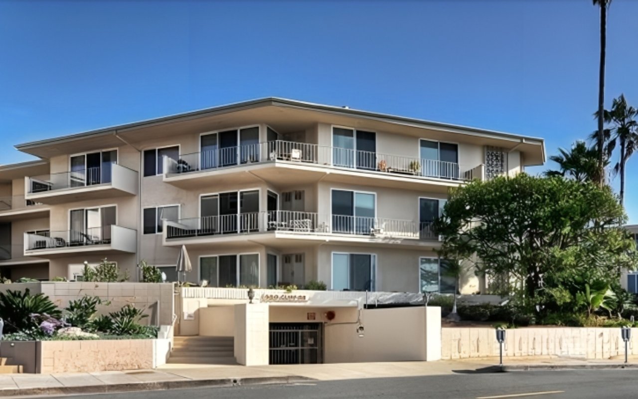 Condominium building with broad balconies, a gated entrance, and landscaped grounds.