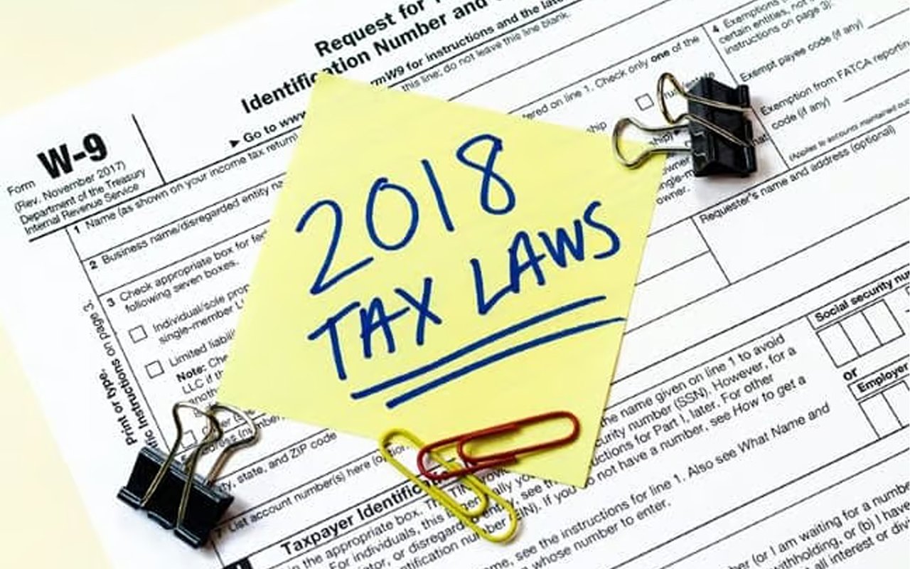 Sticky note reading “2018 TAX LAWS” on a Form W-9 tax document with binder clips and paper clips.