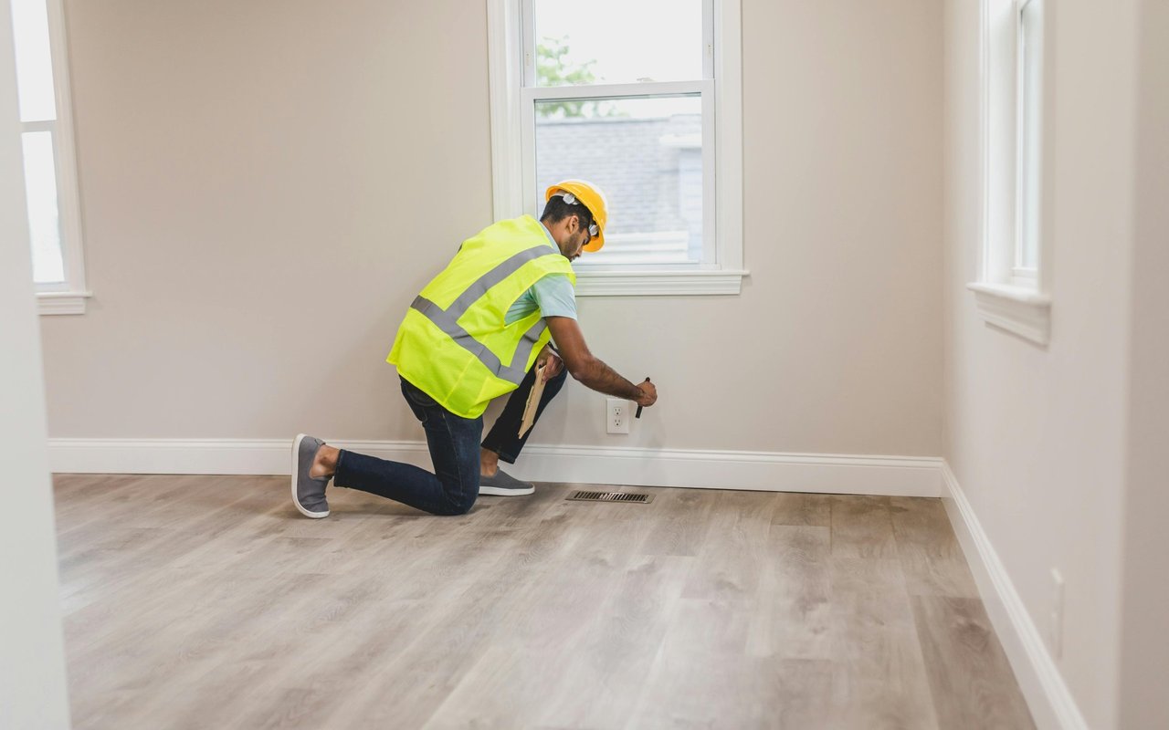 Home inspector kneels to examine an electrical outlet in an empty room.