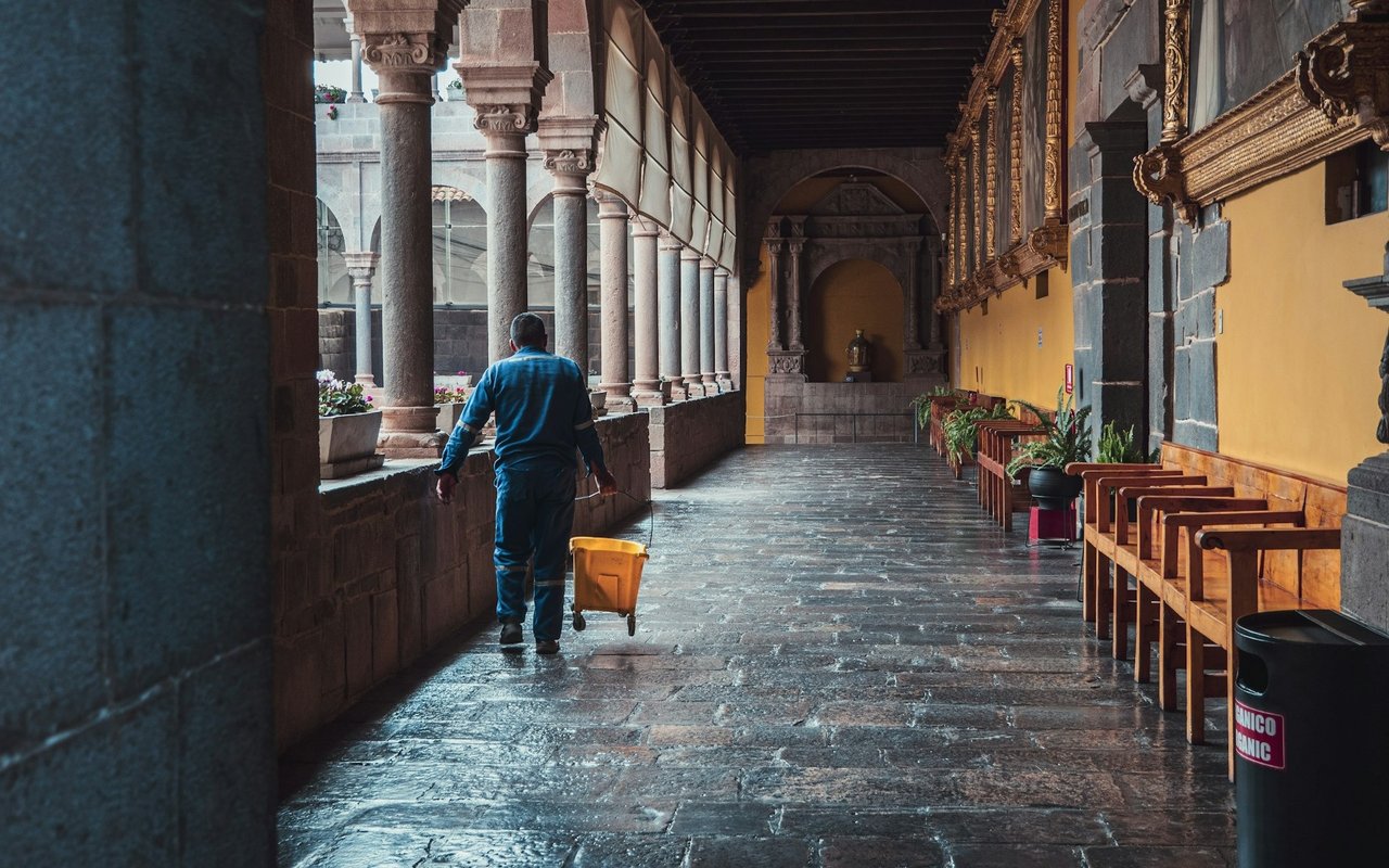 Commercial corridor with stone columns and wooden chairs as a worker cleans with a mop bucket.