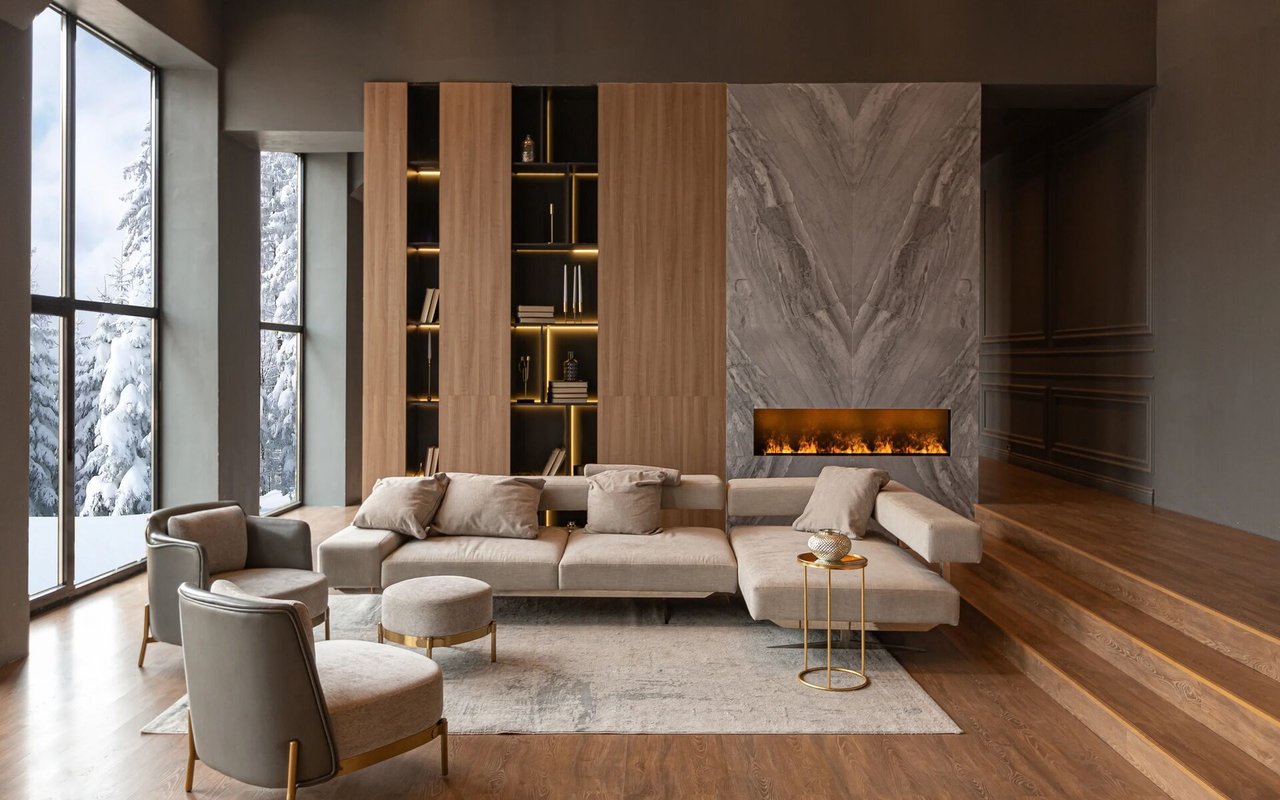 A modern living room with a neutral-toned sectional sofa, a fireplace, and large windows looking out at a snowy landscape.