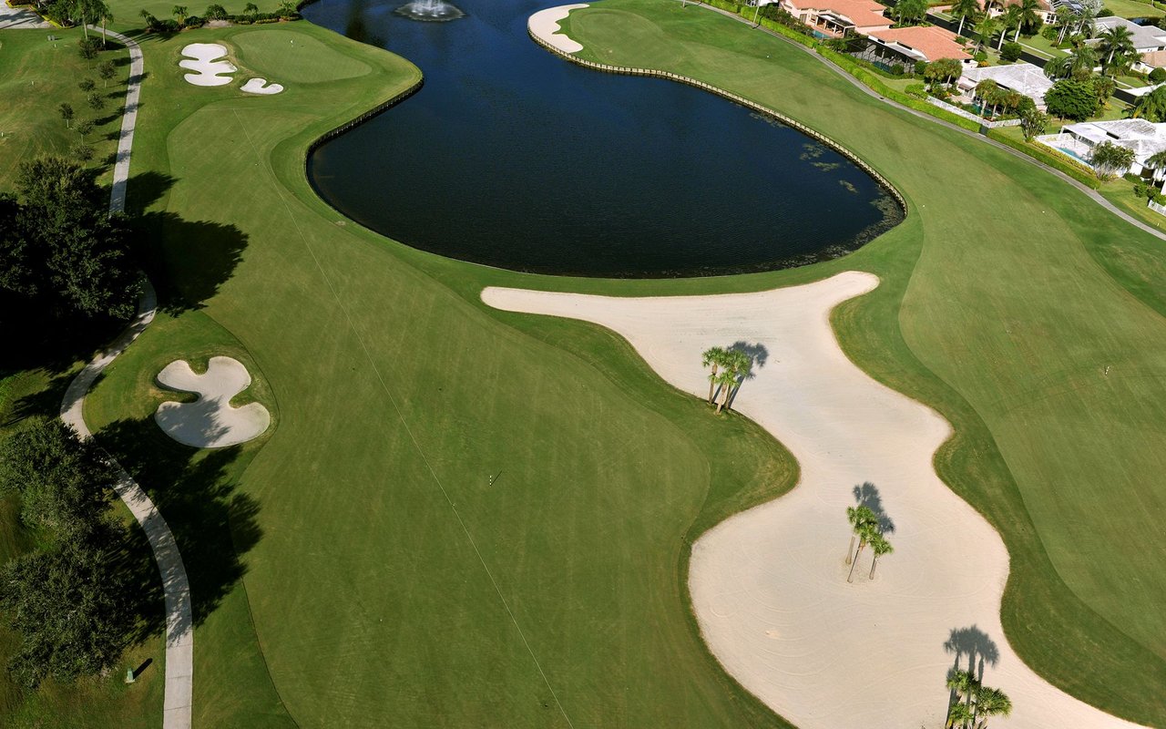 Aerial golf course with sculpted sand bunkers, a lake, and homes along the fairway.