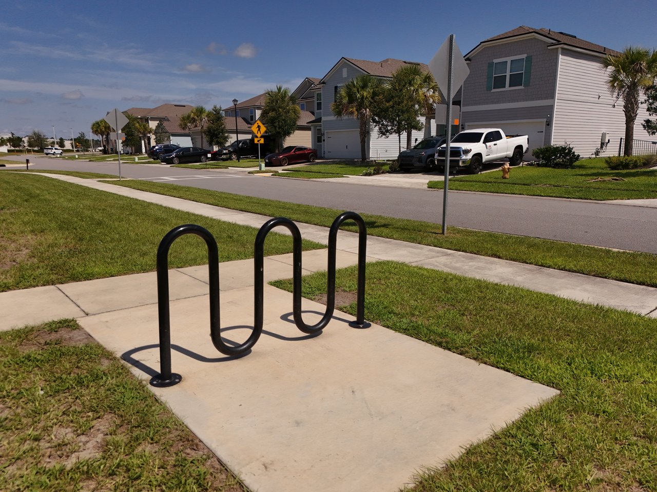 Residential street with detached homes, palm trees, sidewalks, and a bicycle rack.