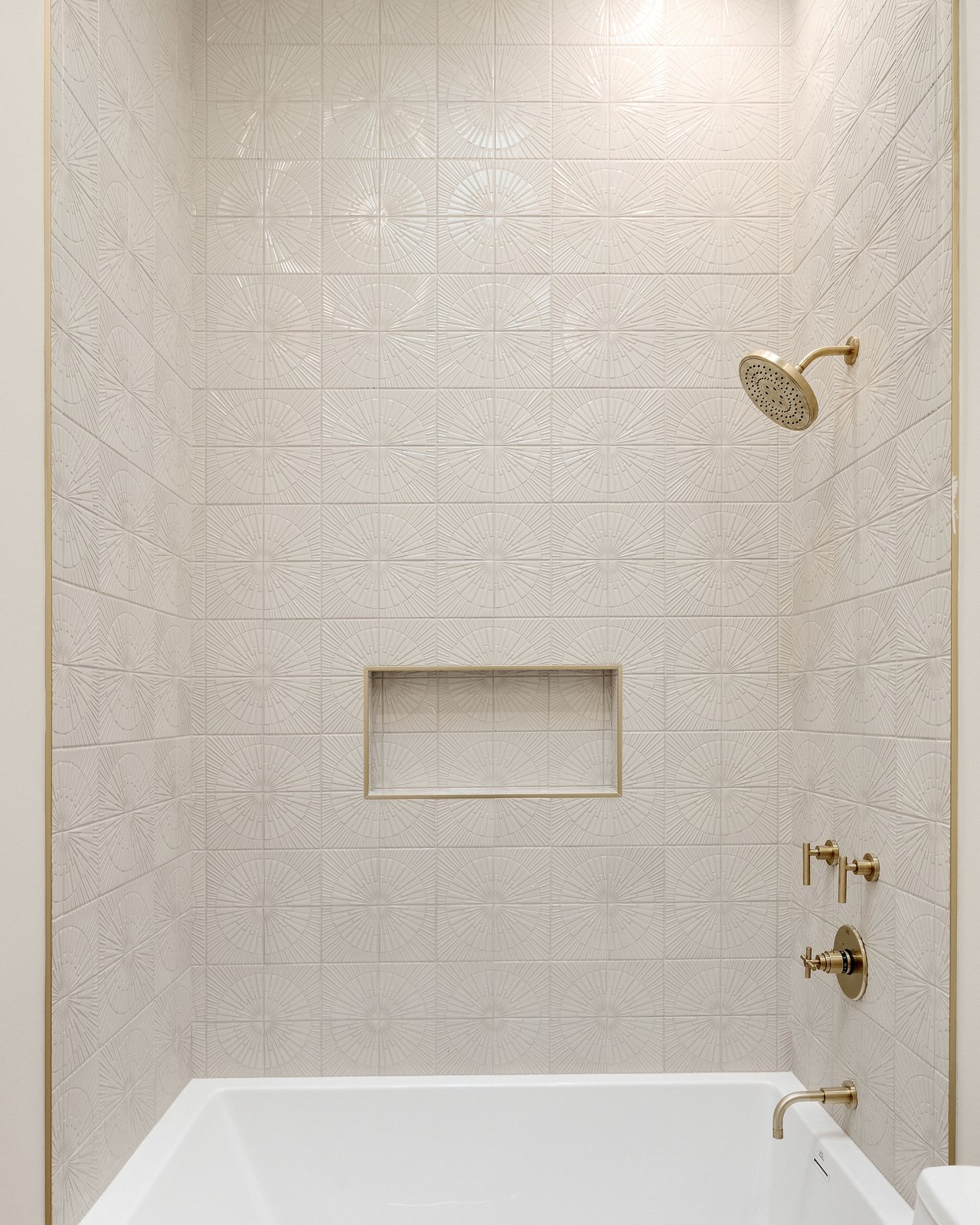 Bathtub shower with patterned white tile, a recessed niche, and brass fixtures.