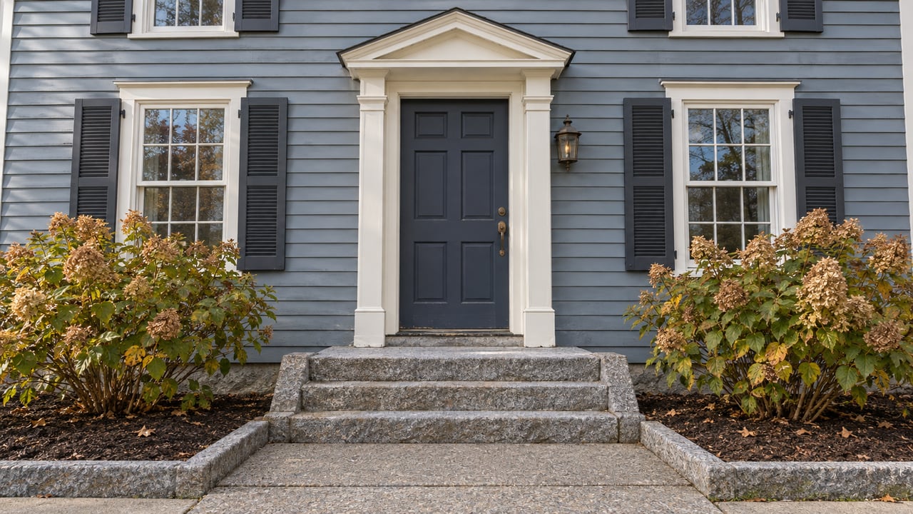 Blue-gray clapboard home with a navy front door, granite steps, ivory trim and two autumn hydrangeas.