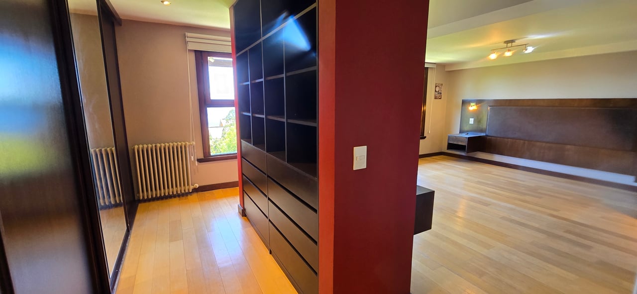 Vacant bedroom with dark built-in wardrobes, a long padded headboard, and light wood flooring.