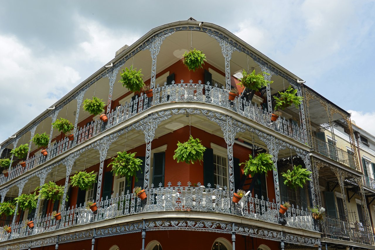 Multi-story red building with ornate white iron balconies and hanging ferns.