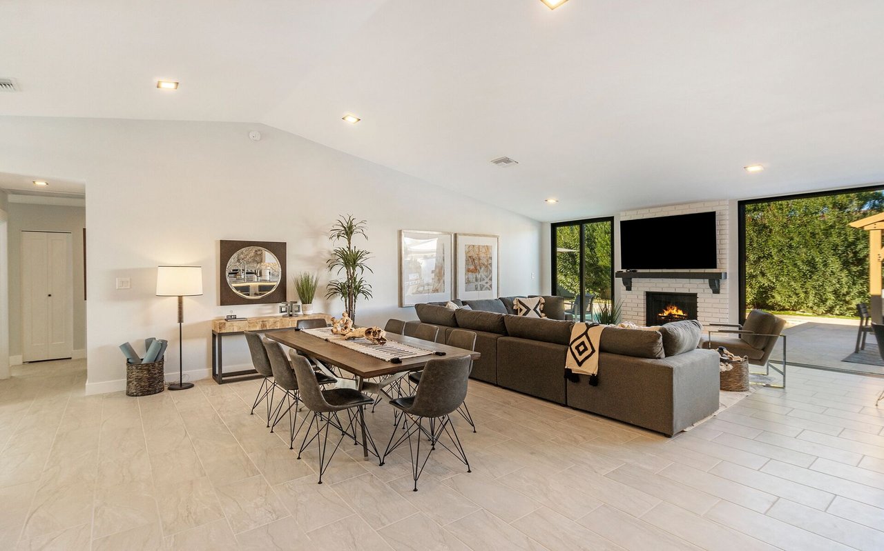 Open-plan living and dining room with a gray sectional, fireplace, and glass doors to the yard.