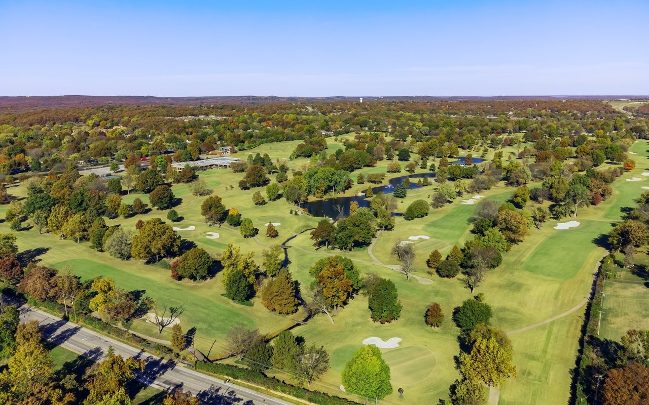 Aerial view of a golf course with tree-lined fairways, sand bunkers, and a pond.