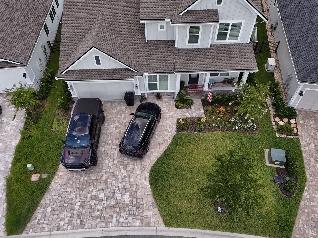 Two-story home with a curved paver driveway, landscaped lawn, and two parked vehicles.