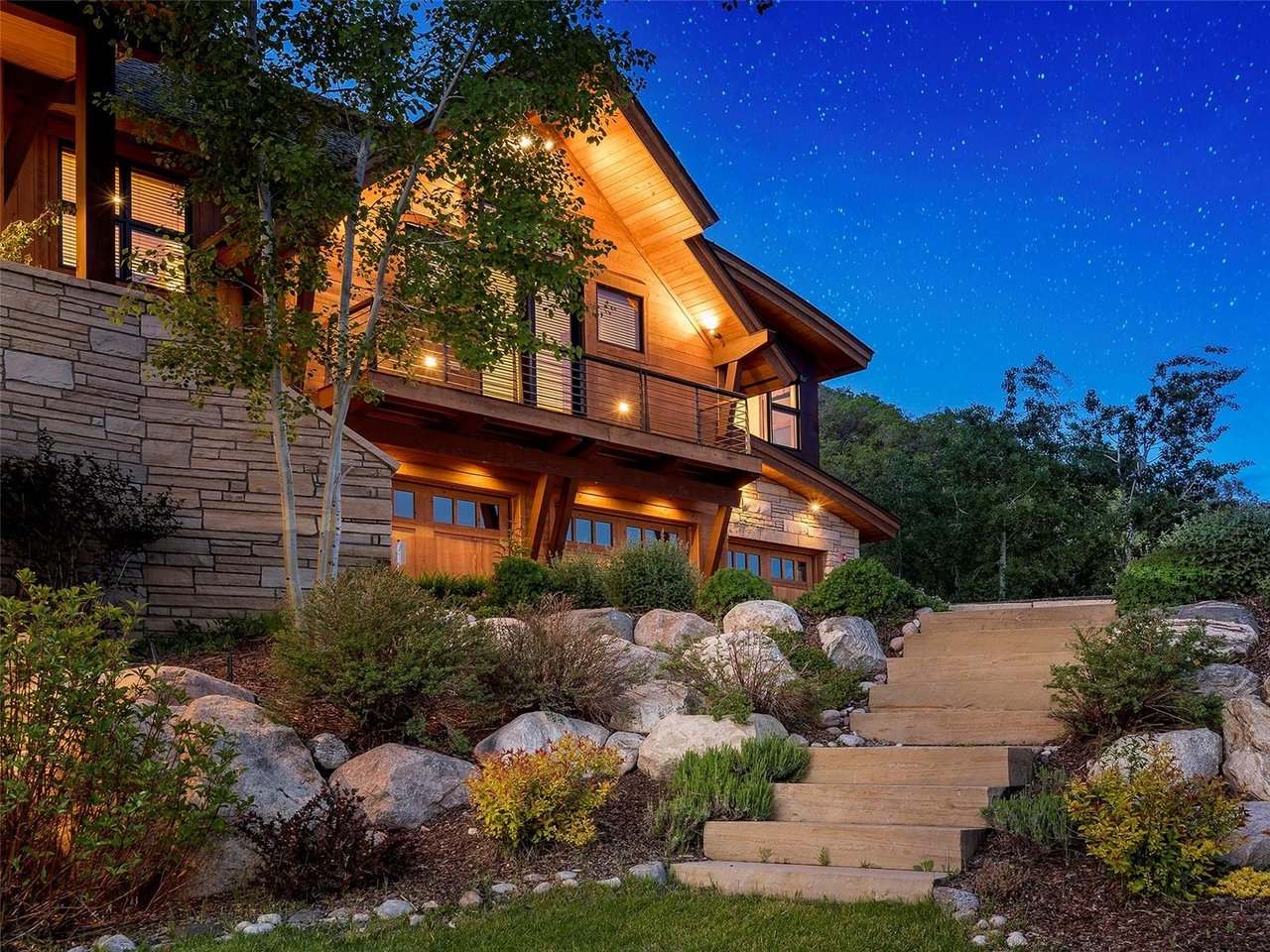 Mountain-style home with warm lighting, stone steps, and a starry night sky.