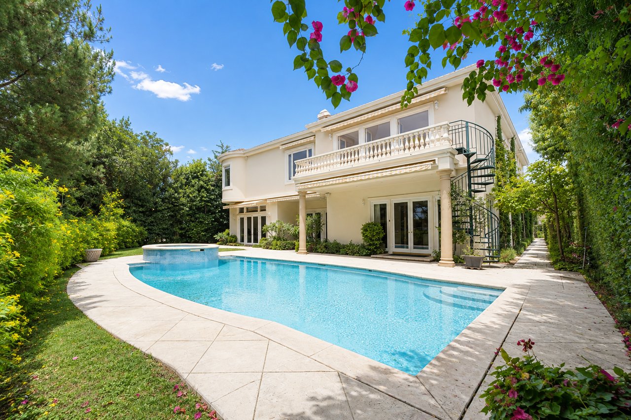 Cream two-story home overlooking a curved pool, with a balcony and spiral staircase.