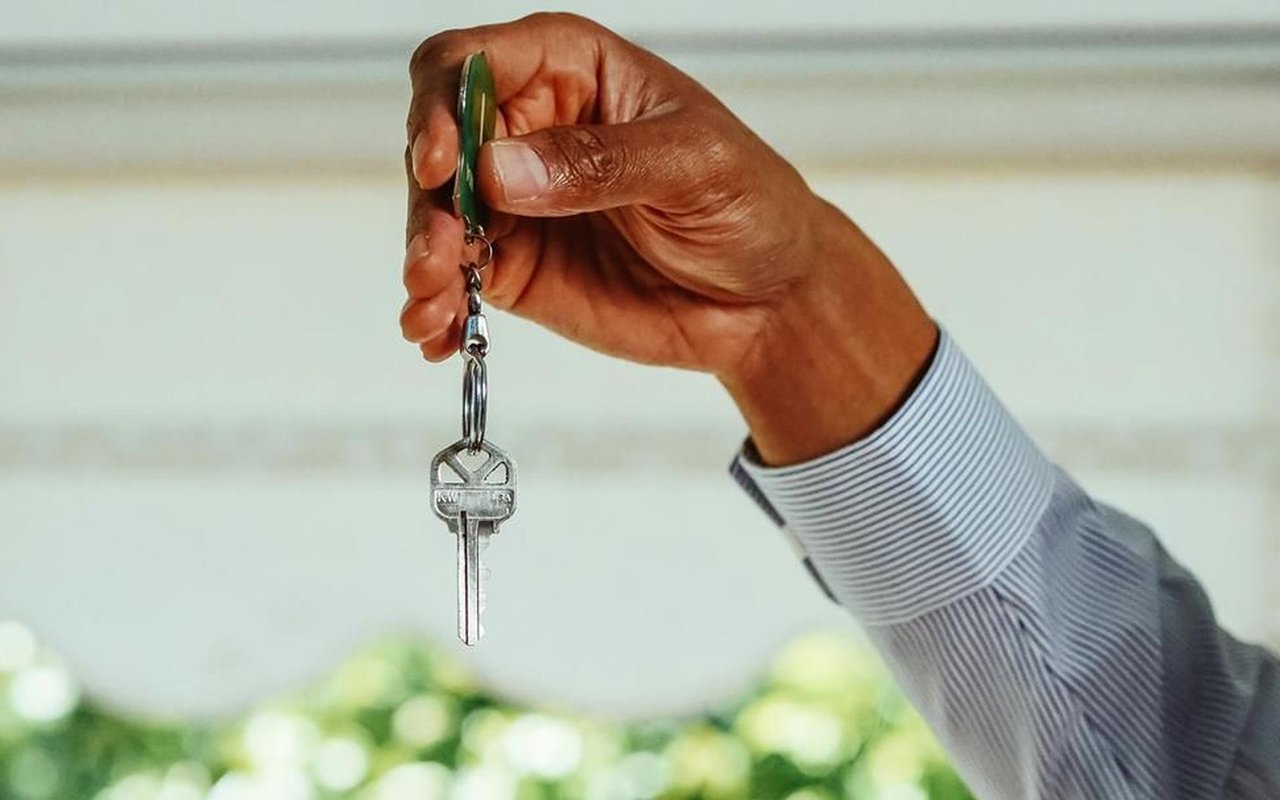 A hand holds a silver house key on a green key ring.