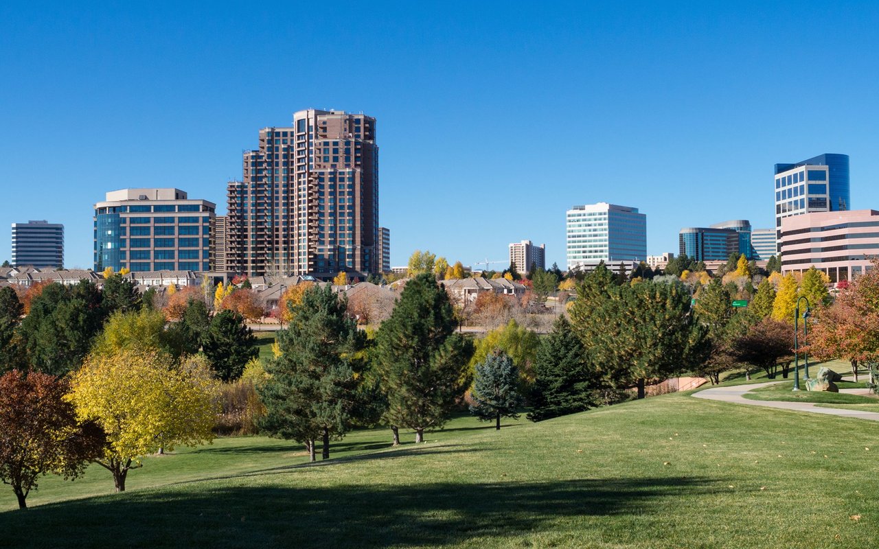Centennial skyline beyond a park with autumn-colored trees and green lawns.