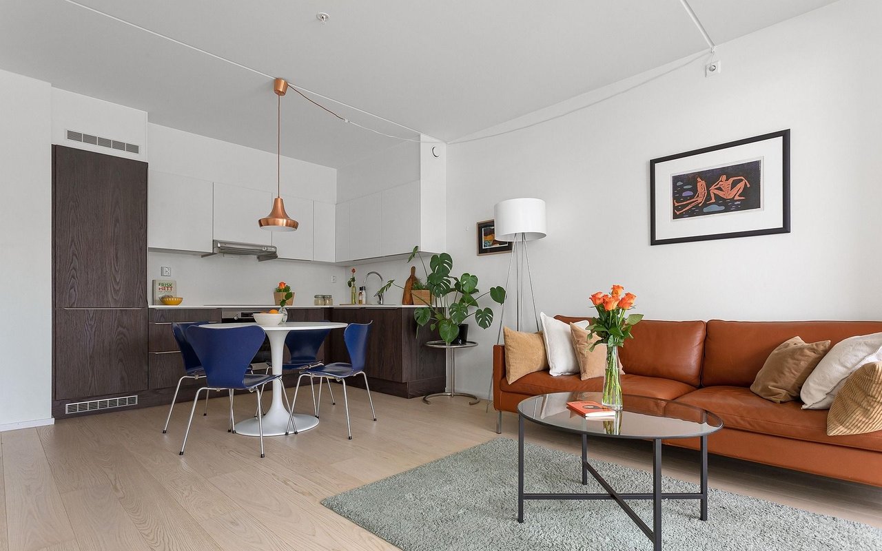 Open-plan living room and kitchen with a rust-colored leather sofa, blue dining chairs, and dark wood cabinetry.