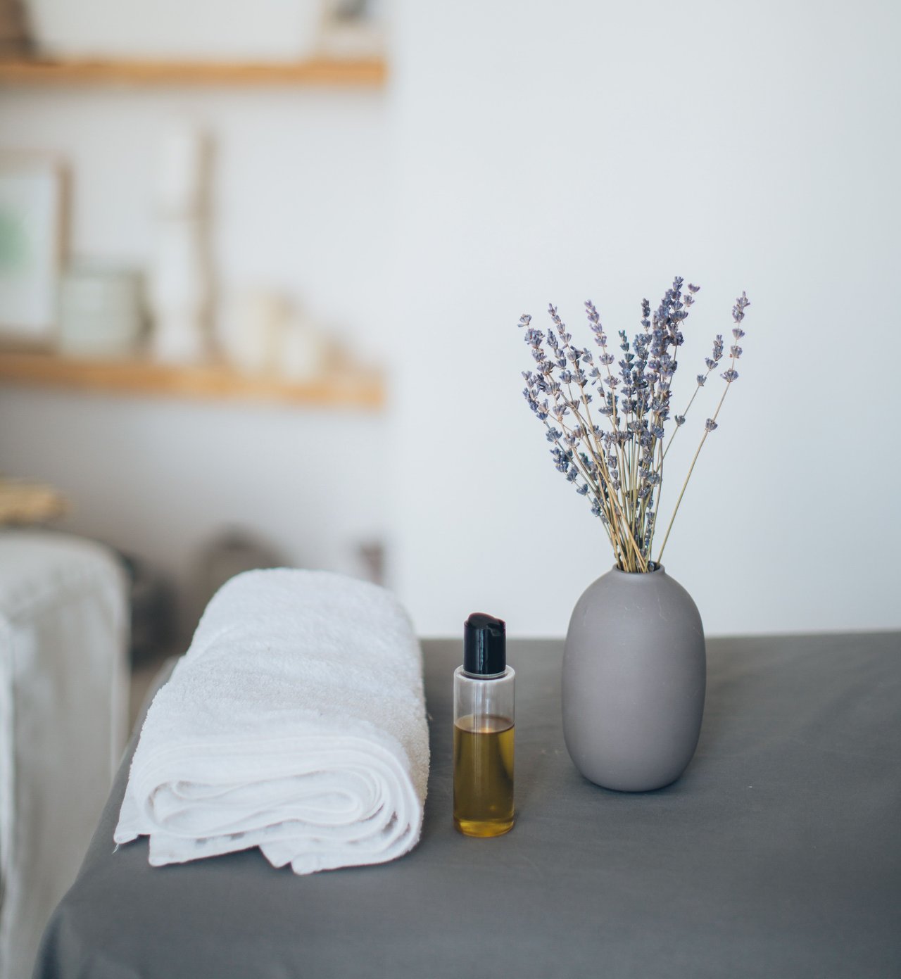 Bathroom vanity with folded white towels, a bottle of oil, and dried lavender in a gray vase.