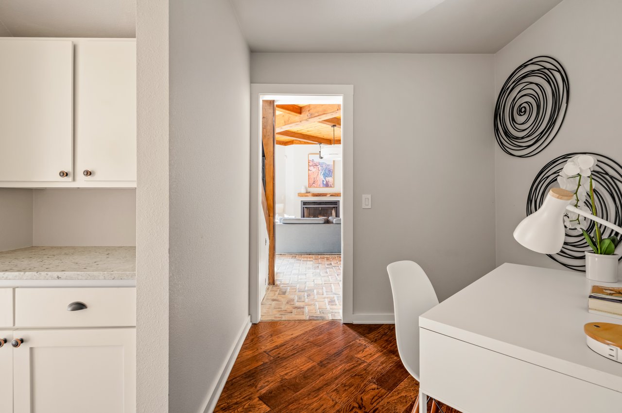 Home office with a white desk, built-in cabinets, and a doorway to the living area.